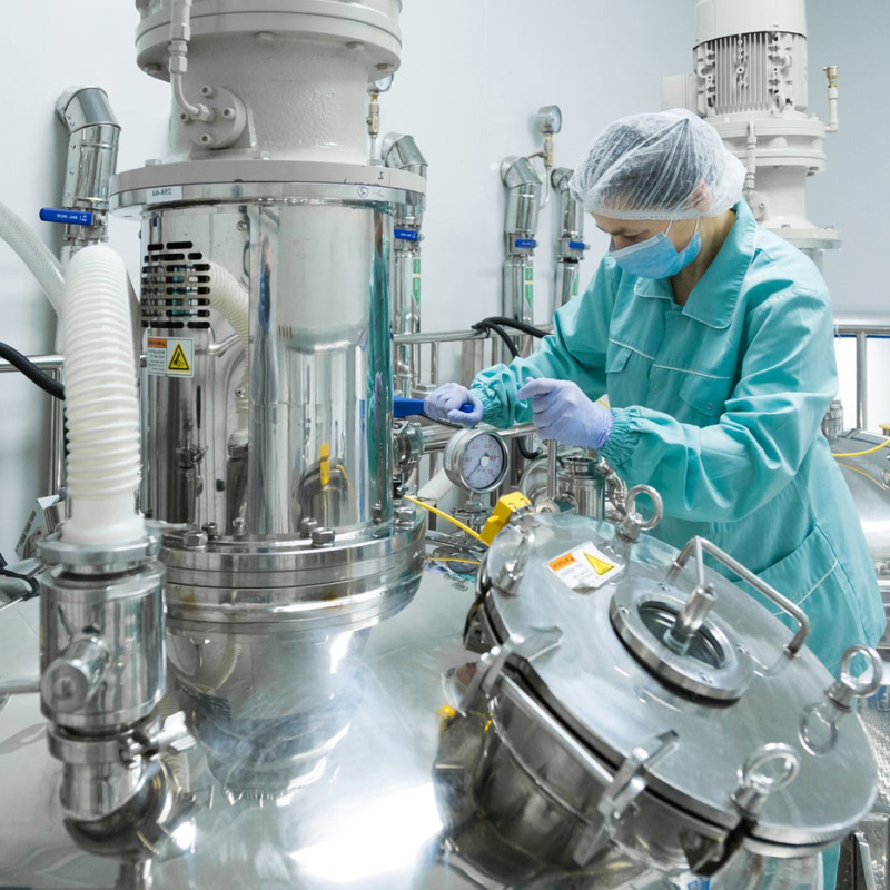 Female technician in PPE working in a pharmaceutical manufacturing facility operating industrial mixing equipment